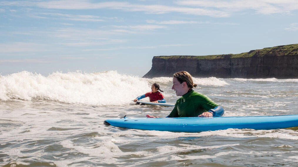 Two women hold onto surf boards waiting for waves in the sea
