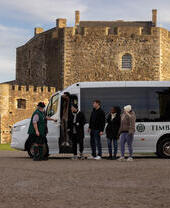 People arriving from a tour bus to visit a castle.