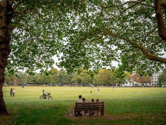 Una familia sentada en un banco con vistas a un parque en verano.