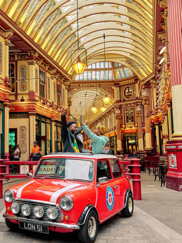 Man and woman in a vintage car under an ornate decorated gold ceiling in a market hall