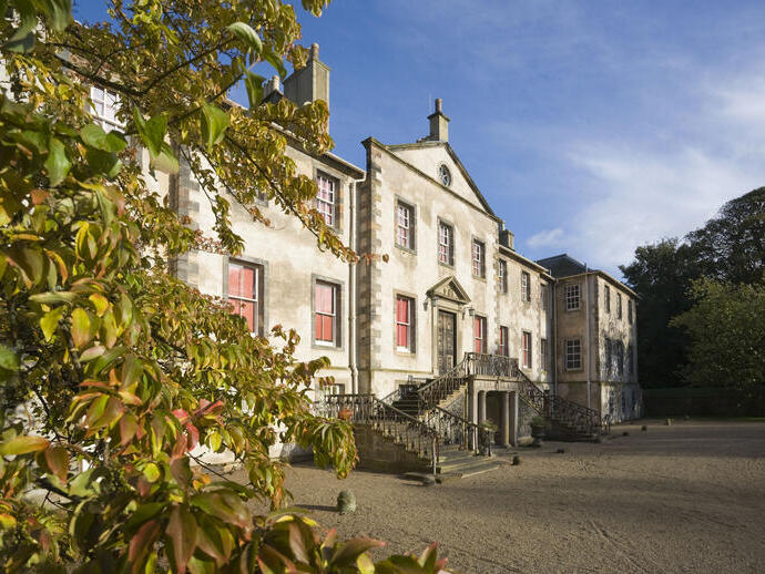 Exterior of a light-brick stately home with staircase entrance, framed by foliage.