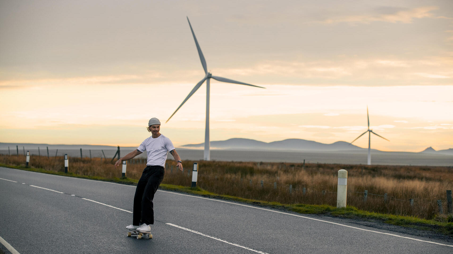 Mann, der auf einer Straße mit Windkraftanlagen im Hintergrund Skateboard fährt