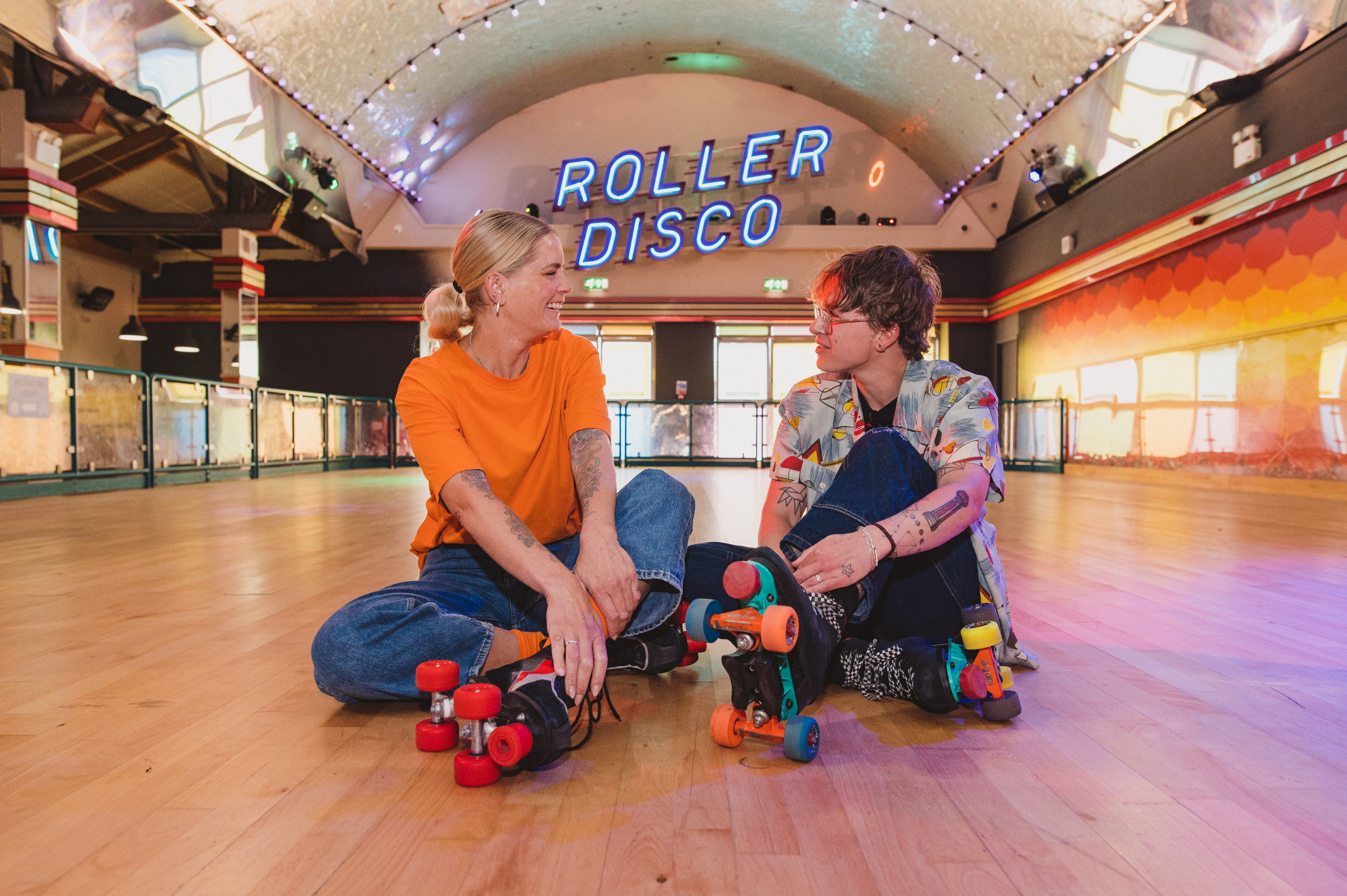 A woman and a man sit wearing roller skates at a Roller Disco