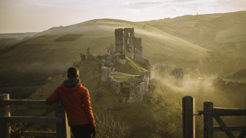 Man leaning on gatepost, looking at the ruins of a castle