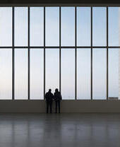 Due persone in silhouette che guardano fuori da un'ampia finestra in un edificio contemporaneo