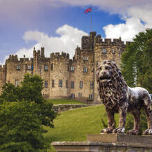 An historic castle with a UK flag at full mast and with a lion statue out the front.