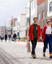 A man and a woman walk along a shopping street with bags