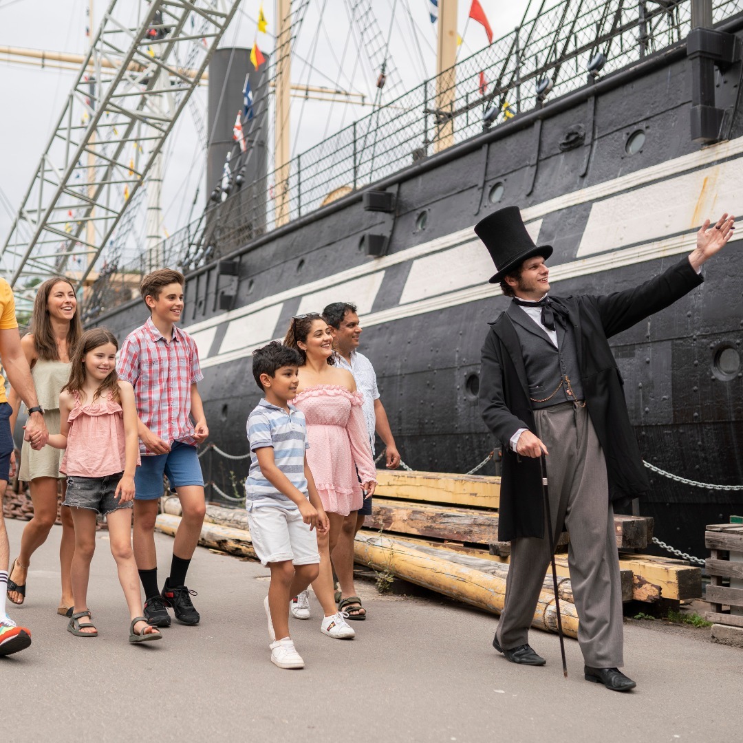 Guide dressed up in 19th century costume showing historic ship to a group of visitors