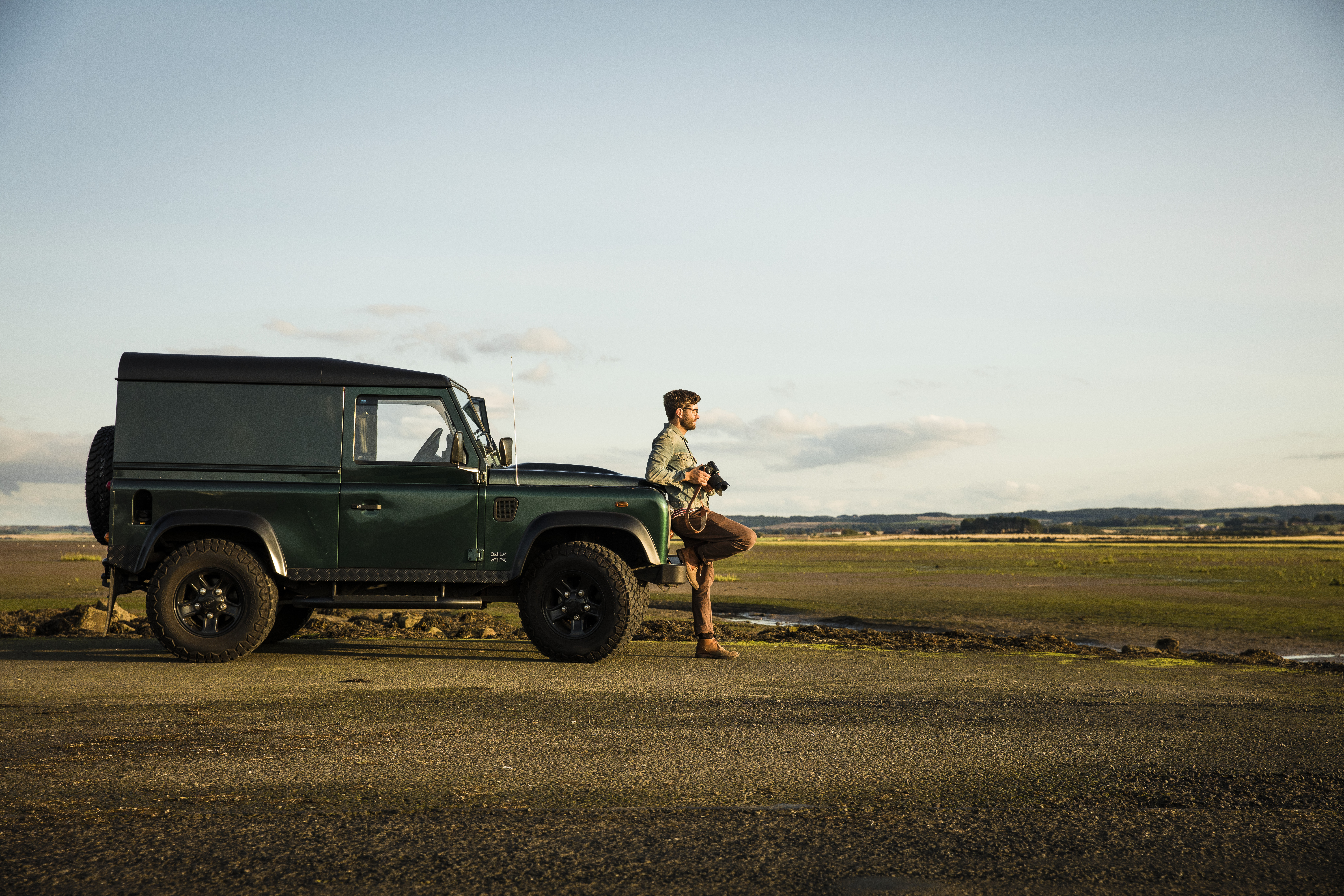Mann, der sich an ein Fahrzeug lehnt und eine Kamera hält