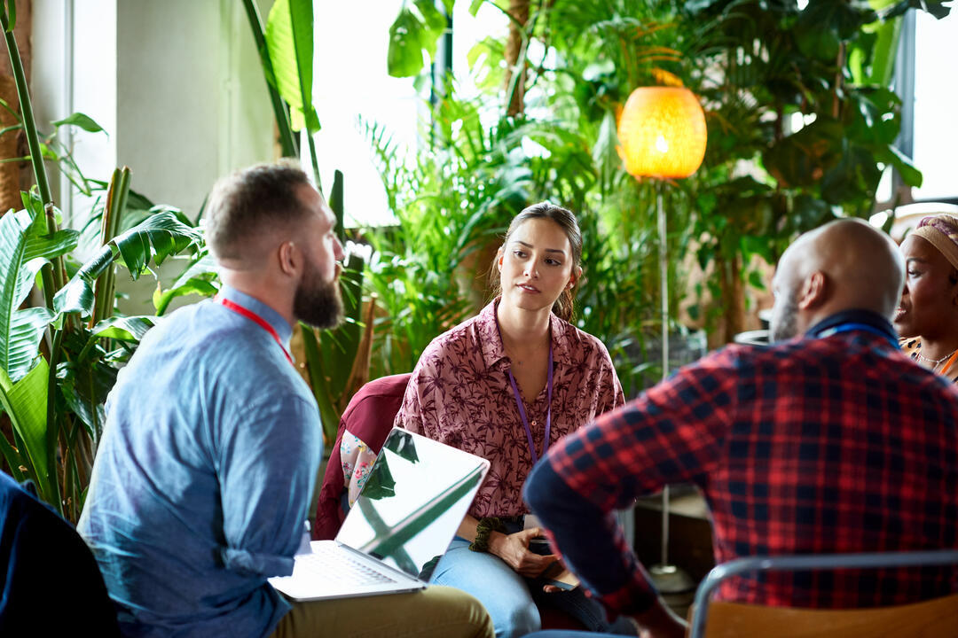 Two men and two women sitting and having a meeting, one of the men is an arm amputee and has a laptop resting on his legs.