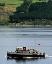A traditional blue and white pleasure boat with a red and black funnel ferrying visitors on a lake.