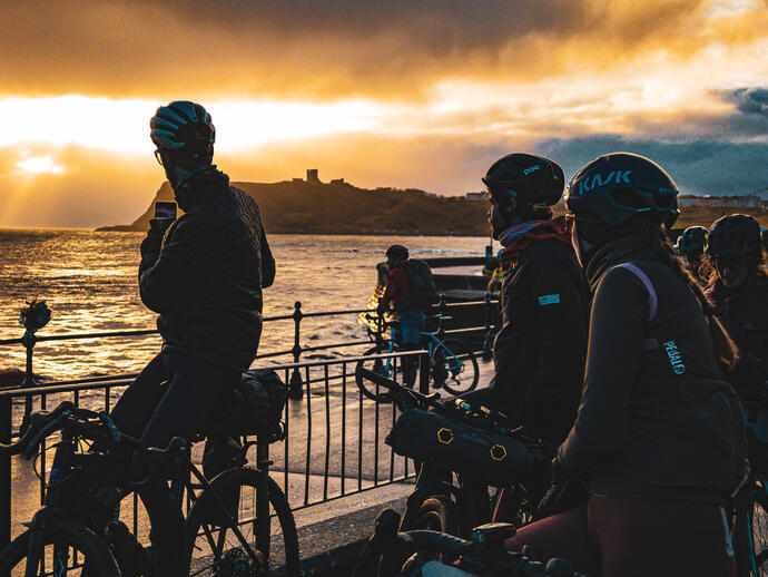 A group of cyclists taking a picture of the sunset on the coast