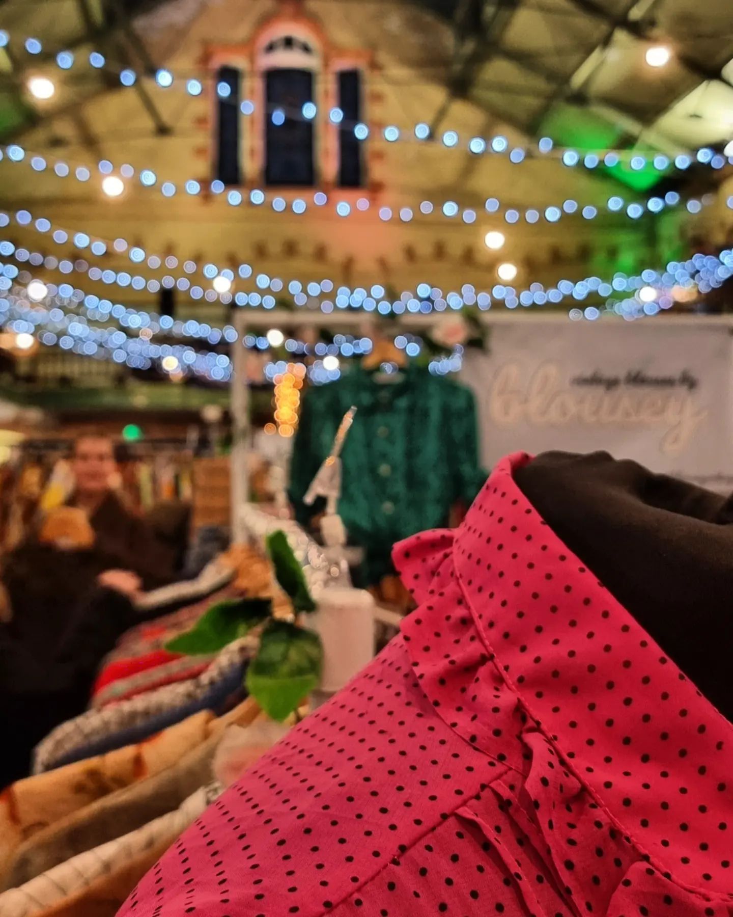 Primer plano de ropa en un puesto del mercado en Victoria Baths con luces de colores al fondo