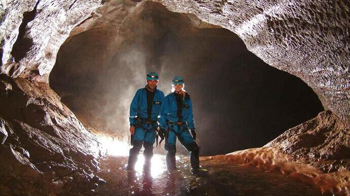 A couple standing in ankle-deep water within a back lit cave