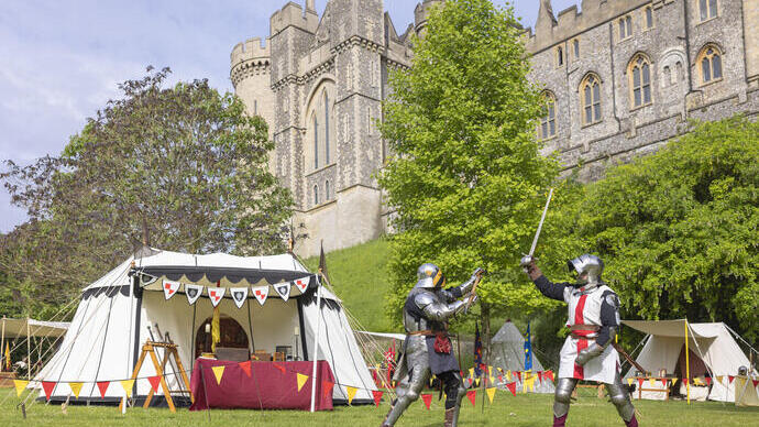 Two men dressed in traditional Armour have a mock sword fight in front of a heritage castle.