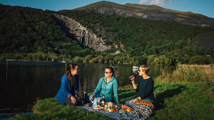 Amigos haciendo un picnic en una pradera junto a un lago de origen glaciar.