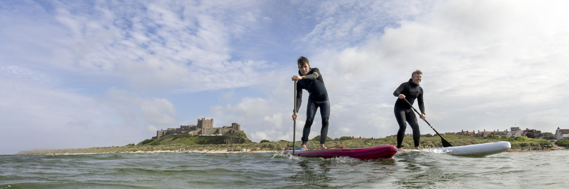 Two men on are paddleboarding in the sea with a heritage castle in the background.