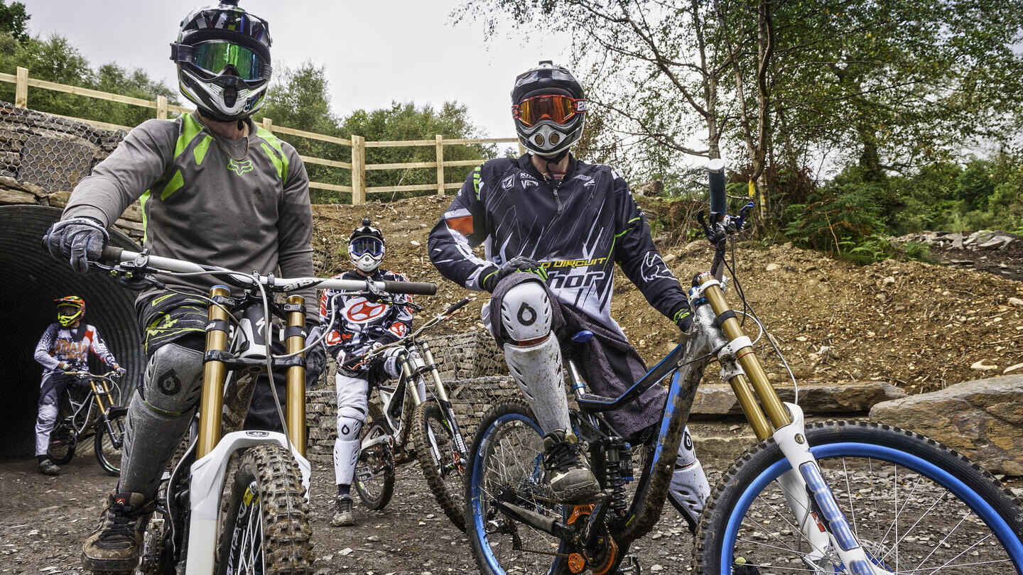 People in gear mountain biking through a tunnel along a muddy path.