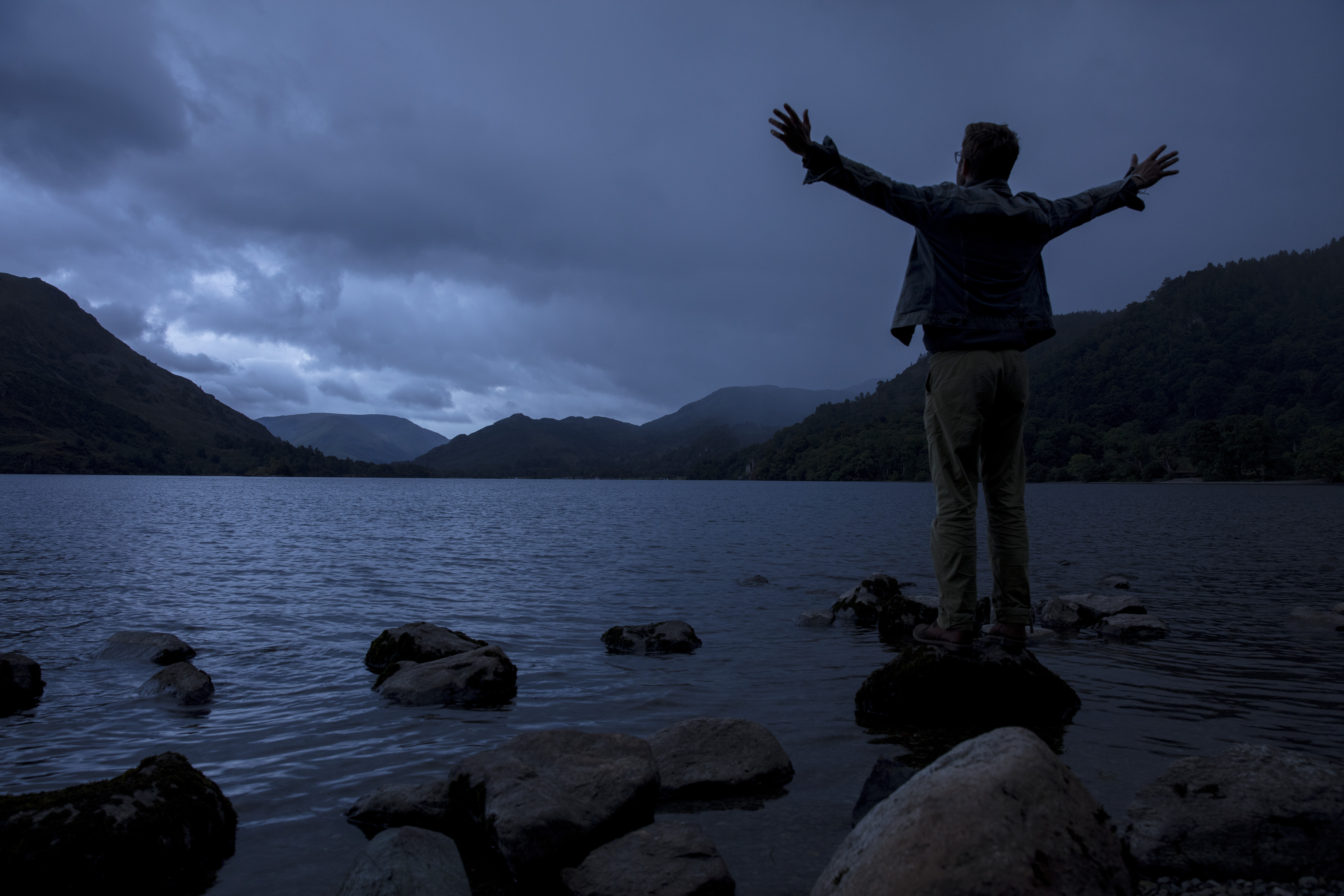 Silhouette of man standing with outstretched arms on shore