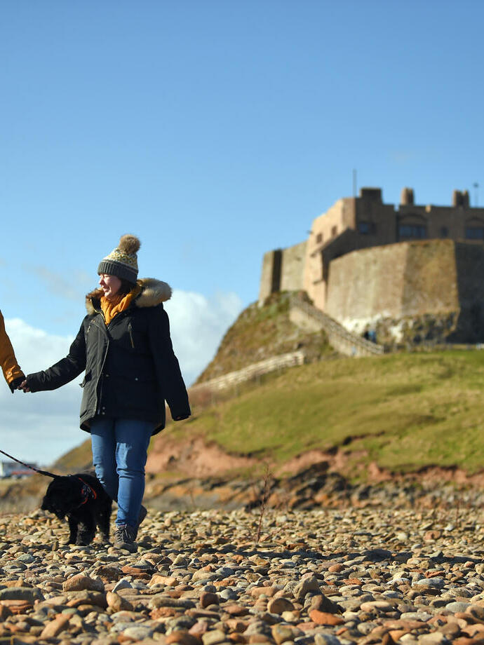 Visitors walking with their dog at Lindisfarne Castle, Northumberland