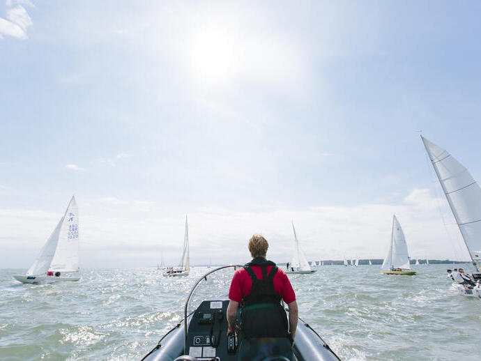 Man steering a power boat during a sailing race with yachts either side