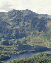 Vue lointaine d'un loch entouré d'arbres et de montagnes verdoyantes.