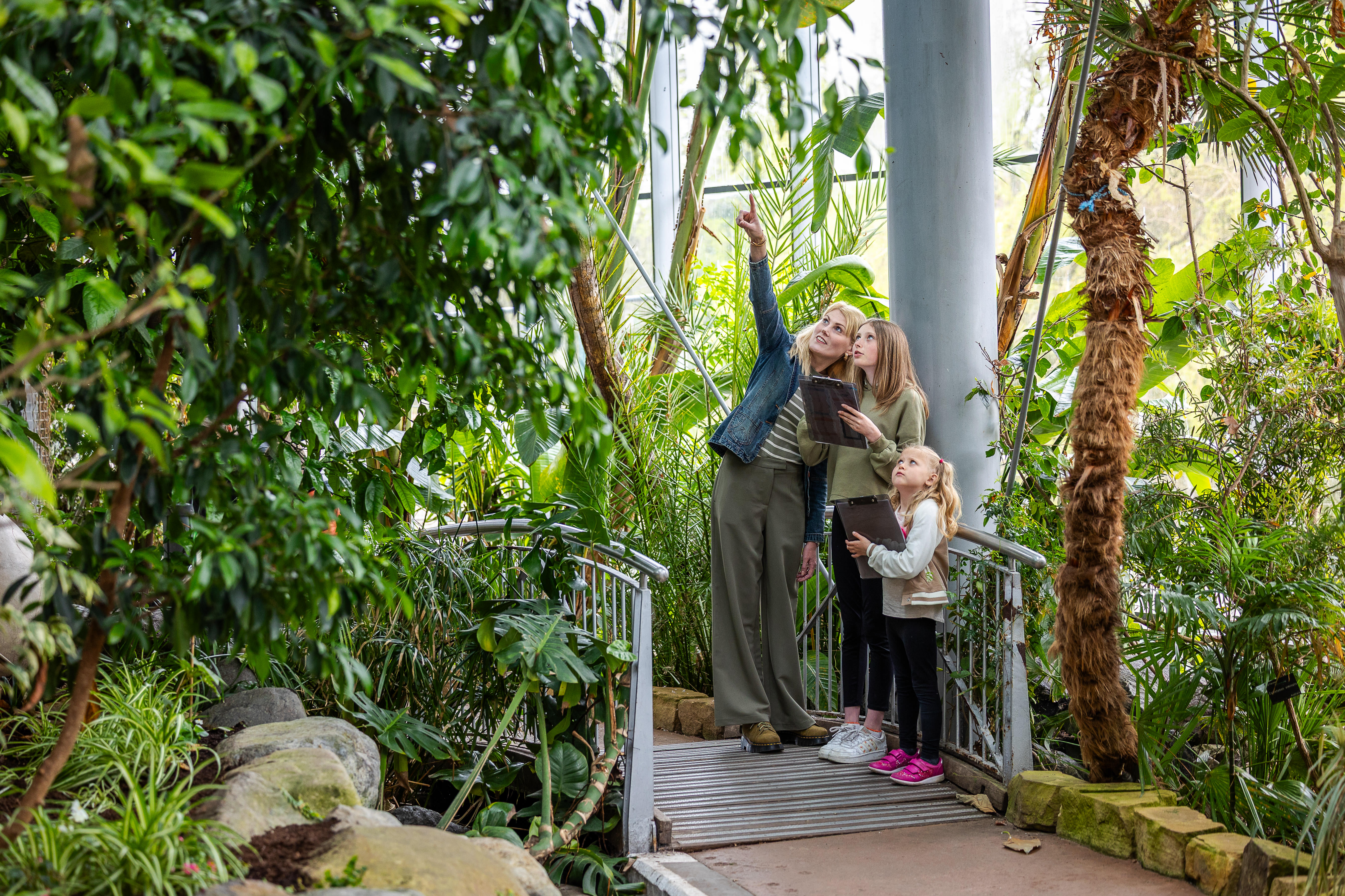 Mum and two girls walking through an enclosed tropical winter garden.