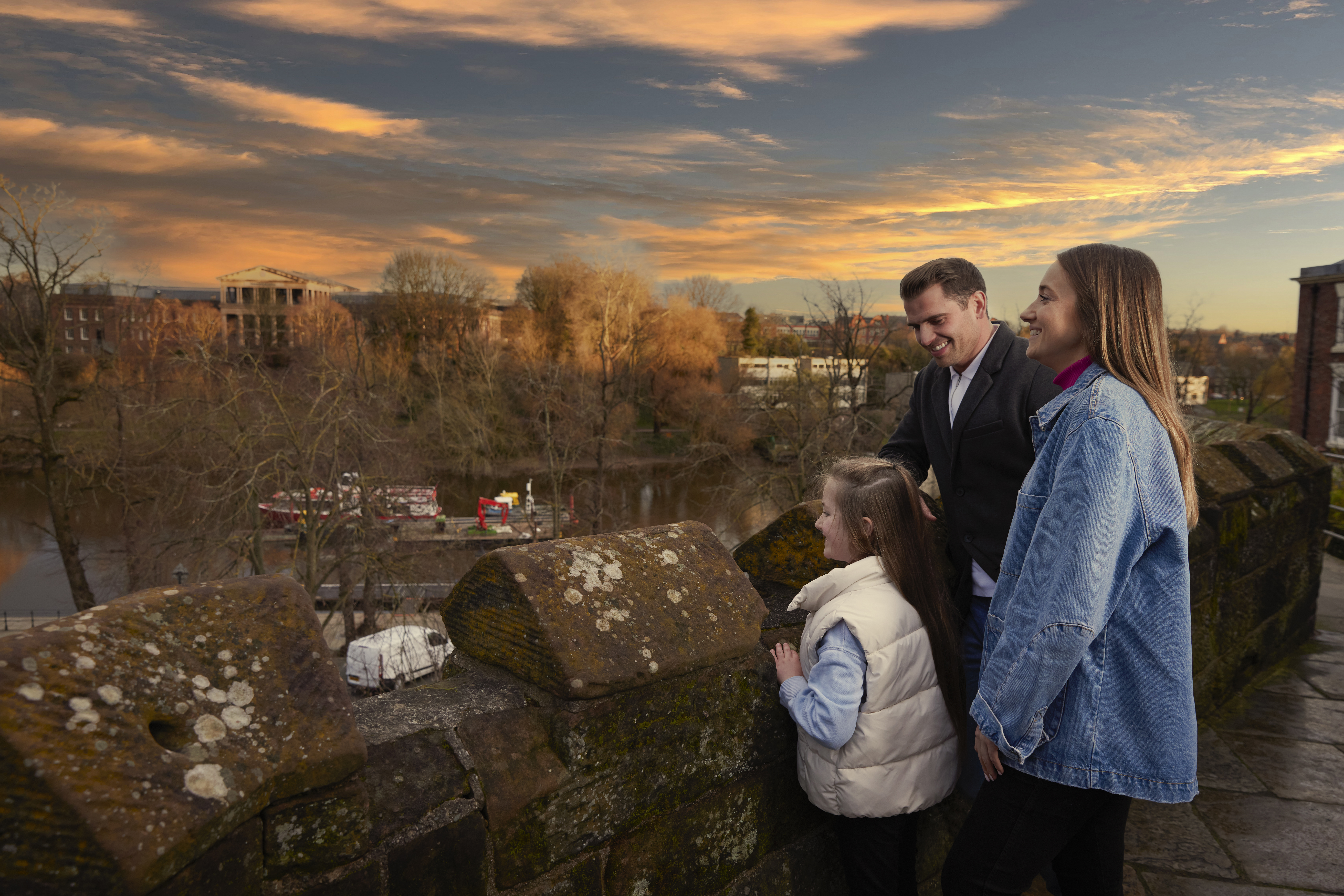 A family of three look out over a town river from a bridge.