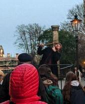 A costumed tour guide on a raised platform in front of an audience next to a historic building.