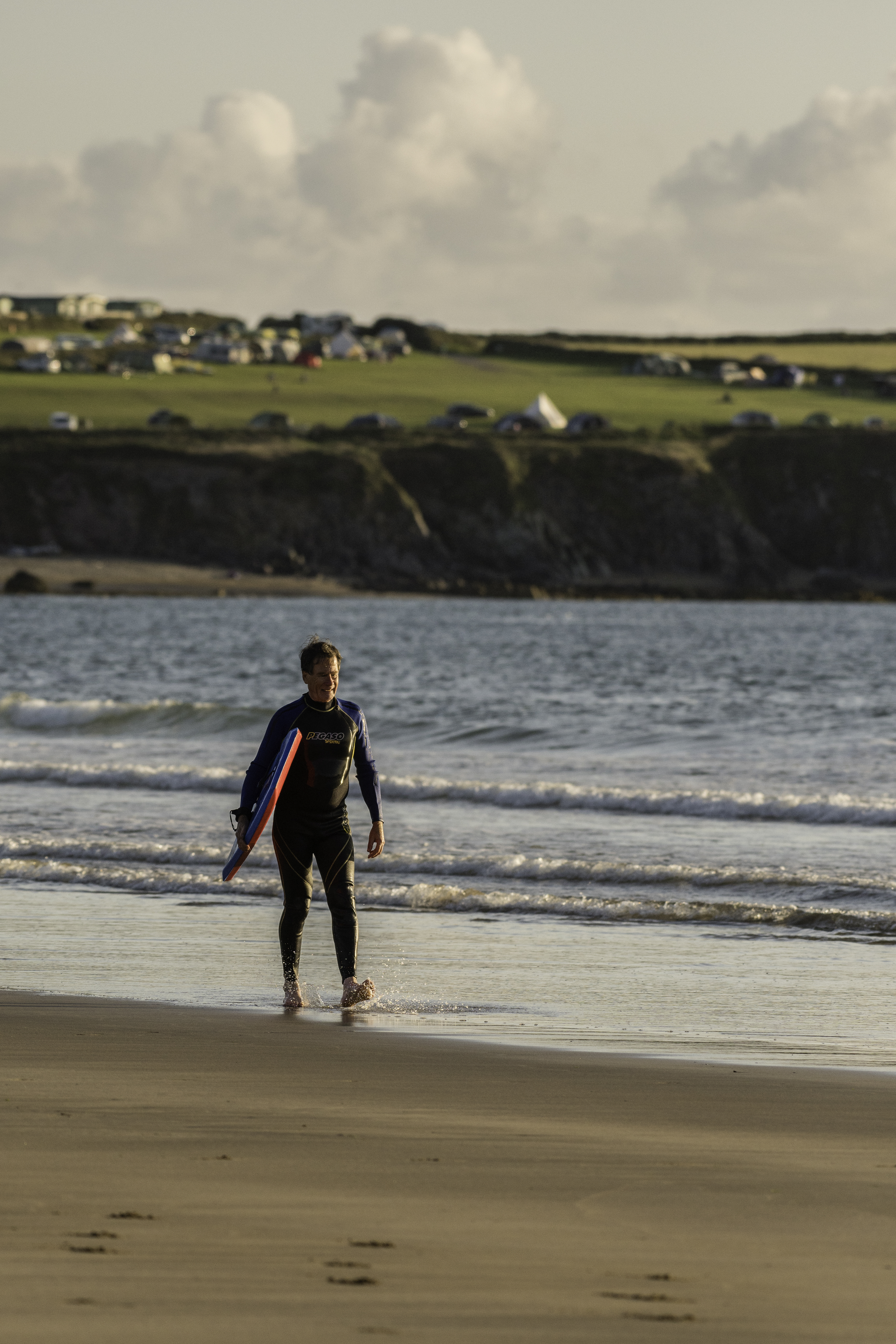 Une personne marchant sur une plage avec une planche de surf sous le bras