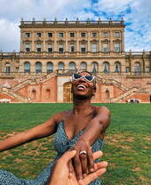 Woman laughing sitting on the grass in front of a stately home