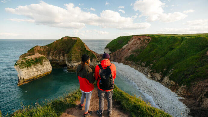 A man and woman stand on a cliff edge in front of a sea view