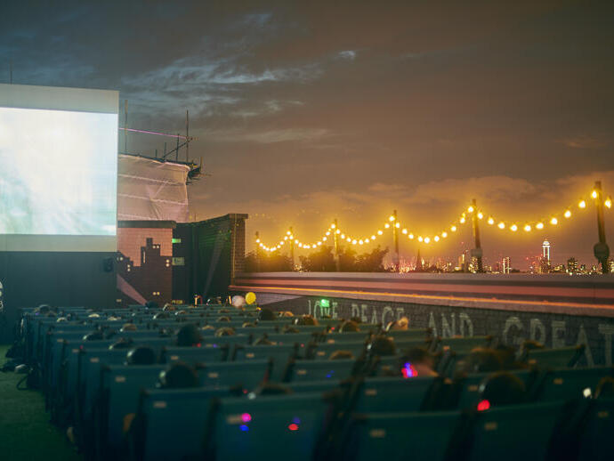 Persone che guardano un film su un grande schermo di notte con lo skyline della città in lontananza