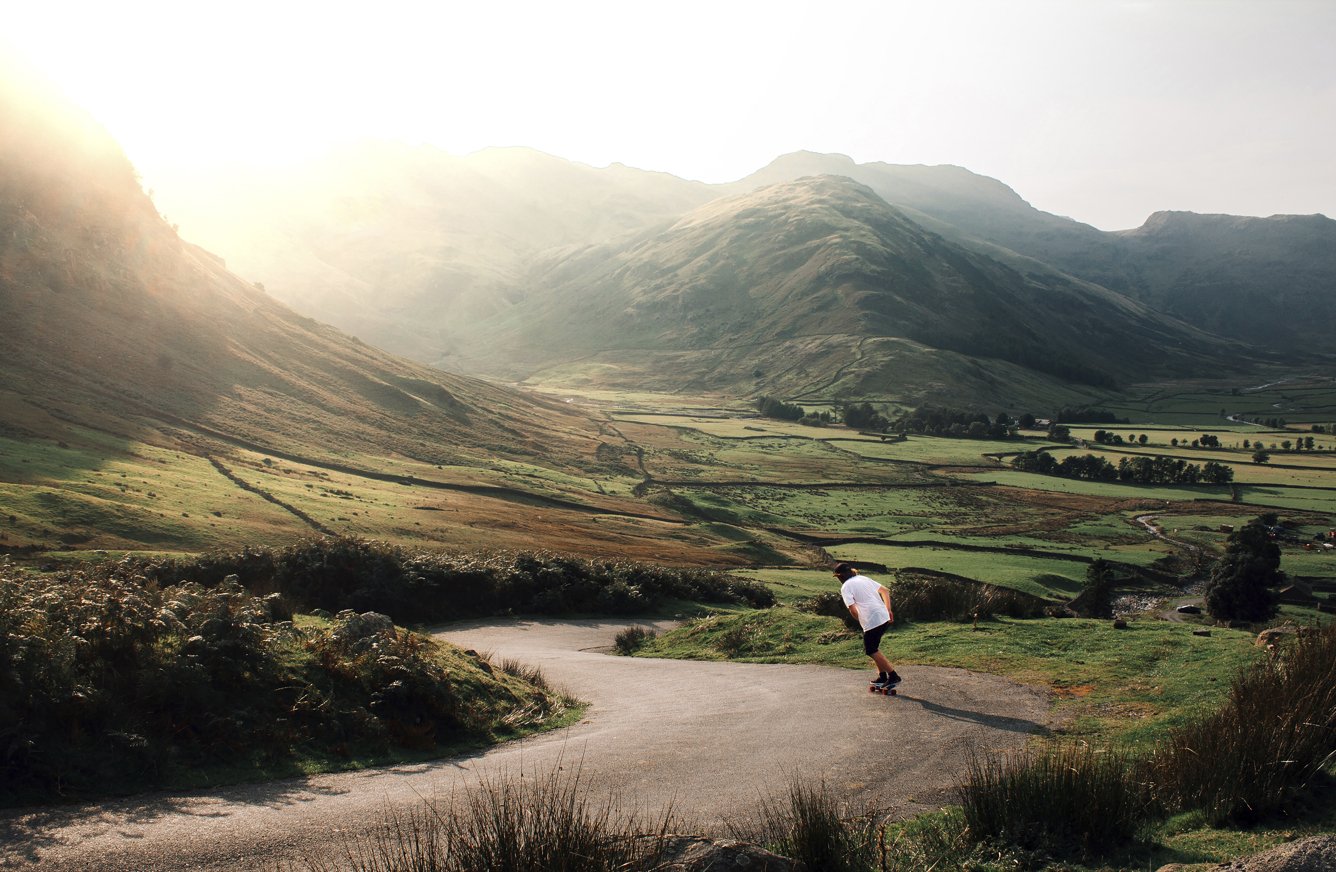 Man skateboarding down a road through a deep valley in the sunshine