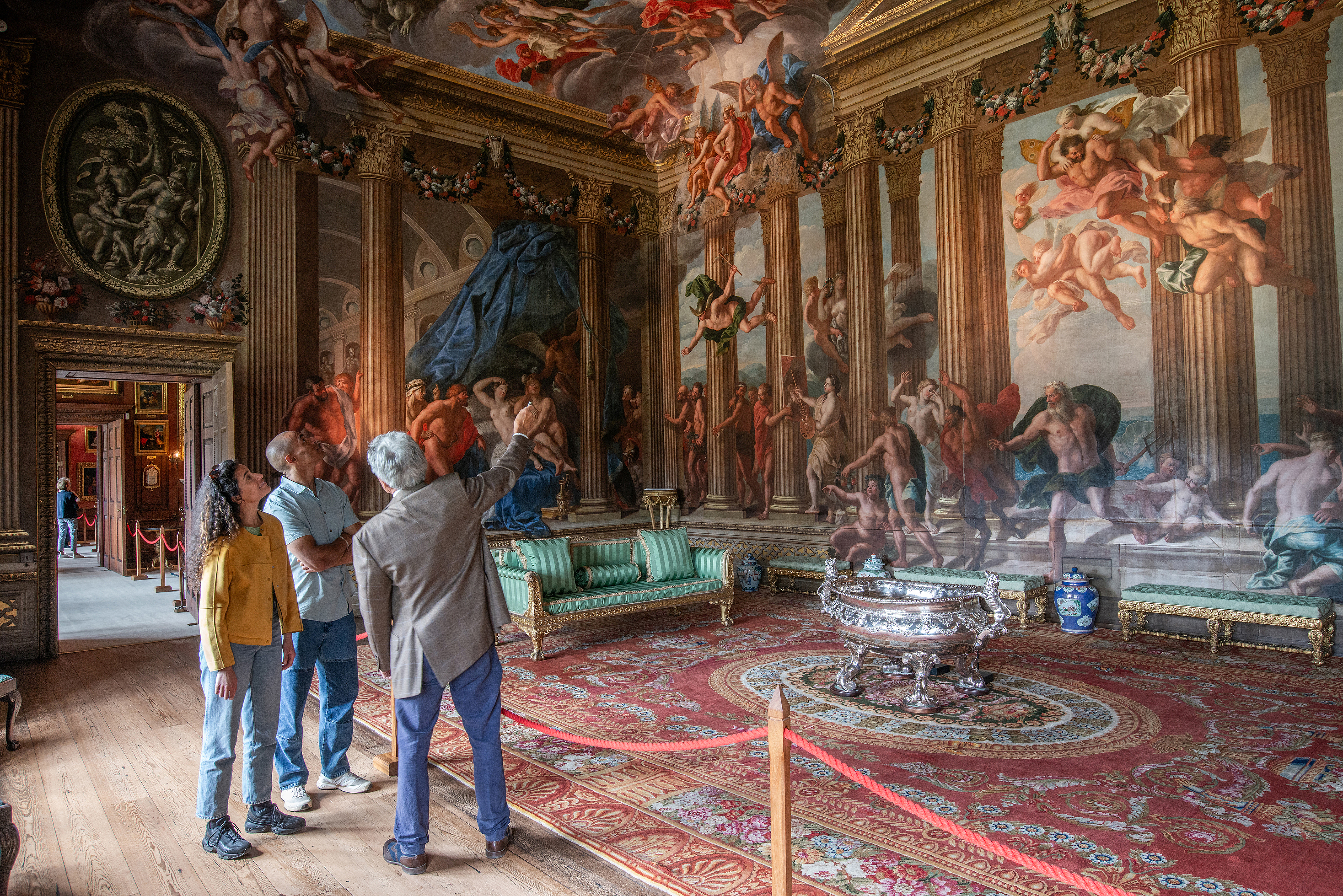 A man and a woman with a tour guide in an ornate room with paintings