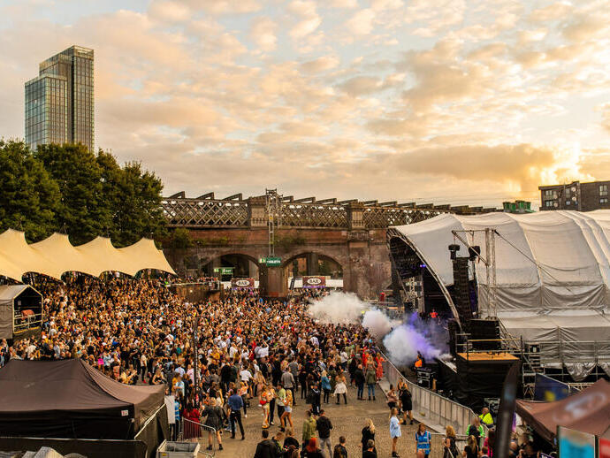 Crowds of people at a festival with stage on right in a city in evening light