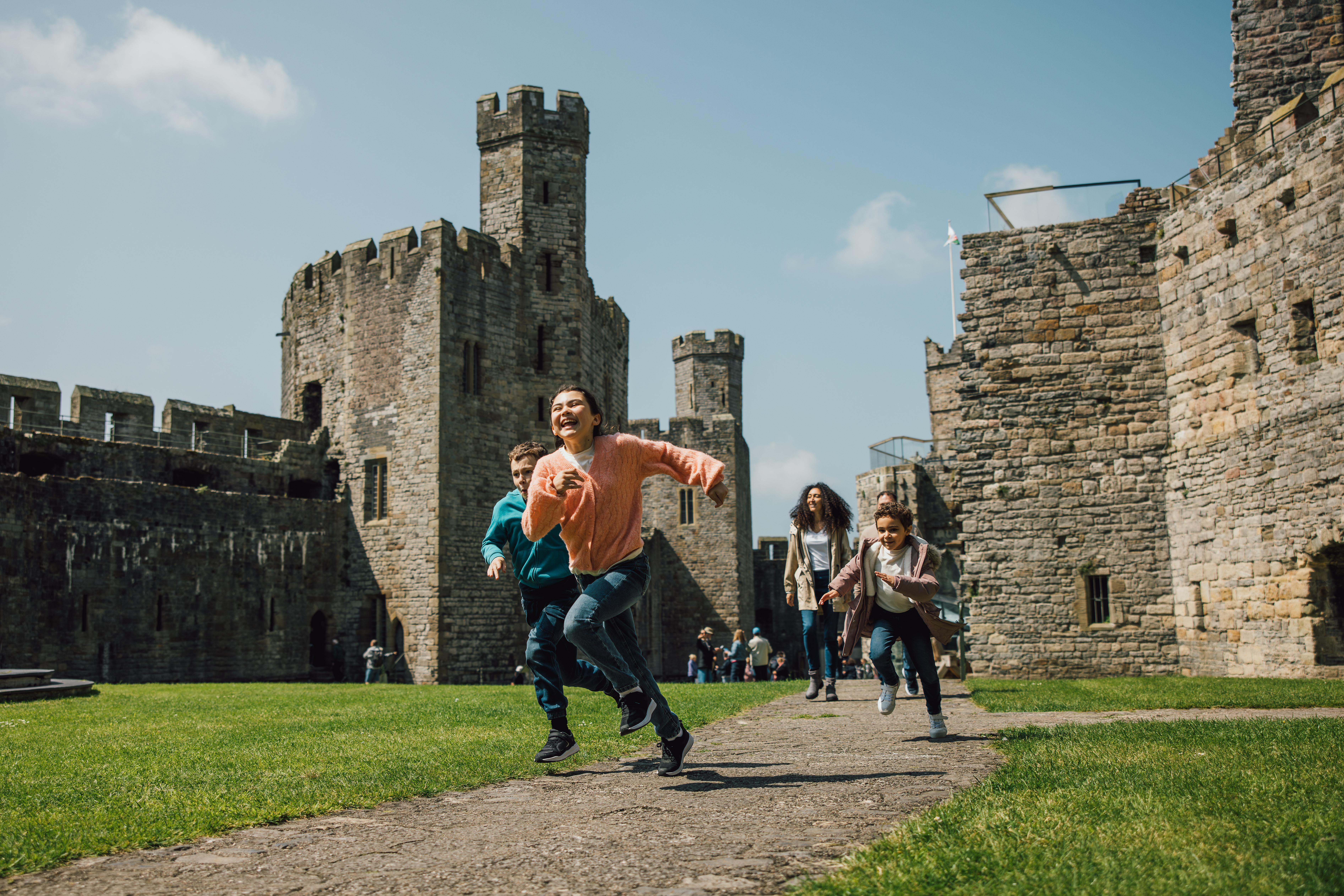 Children running and laughing at a historic stone castle on a sunny day.