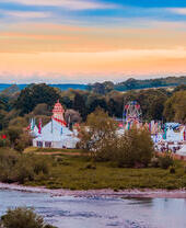 Tents and fairground rides of a summer festival beside a river.
