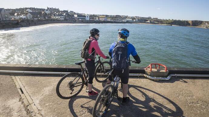 Deux cyclistes sont arrêtés près de la mer et regardent une ville côtière.