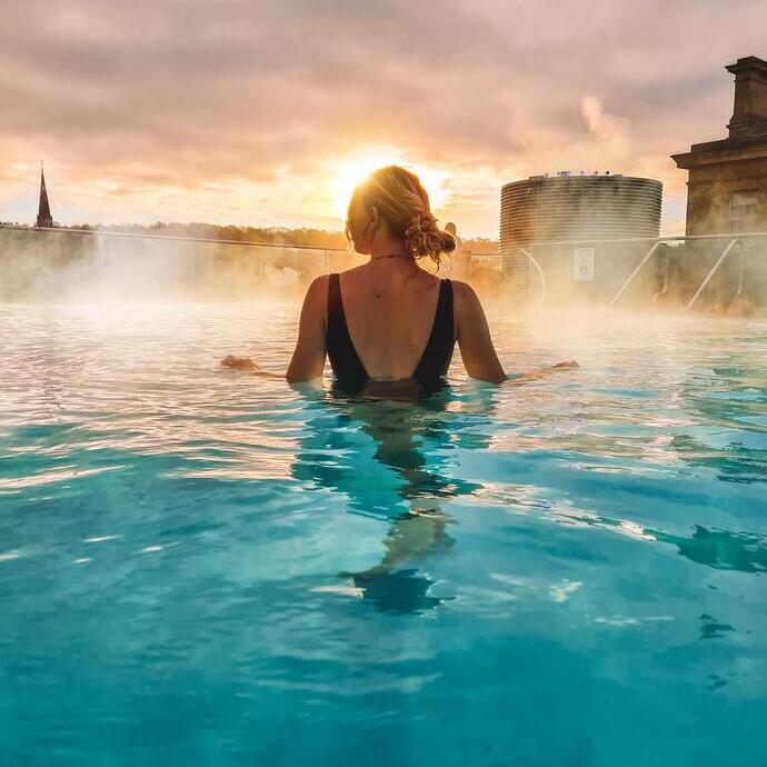 A woman stands looking out to a view in the rooftop pool at sunrise