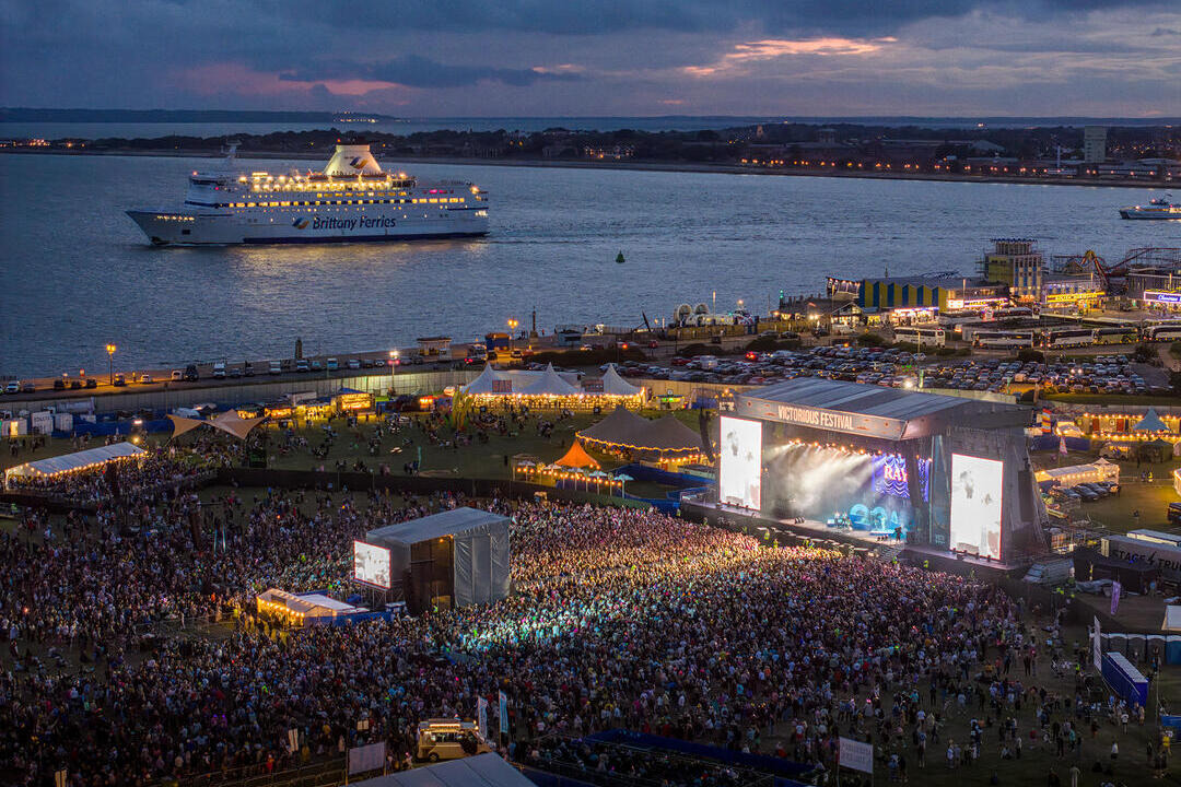 Aerial shot showing crowds at a music festival next to the ocean