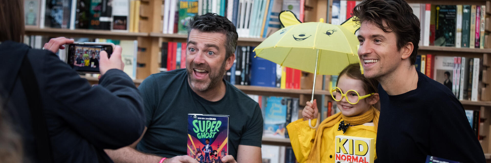 Dos hombres sosteniendo libros y posando con un niño