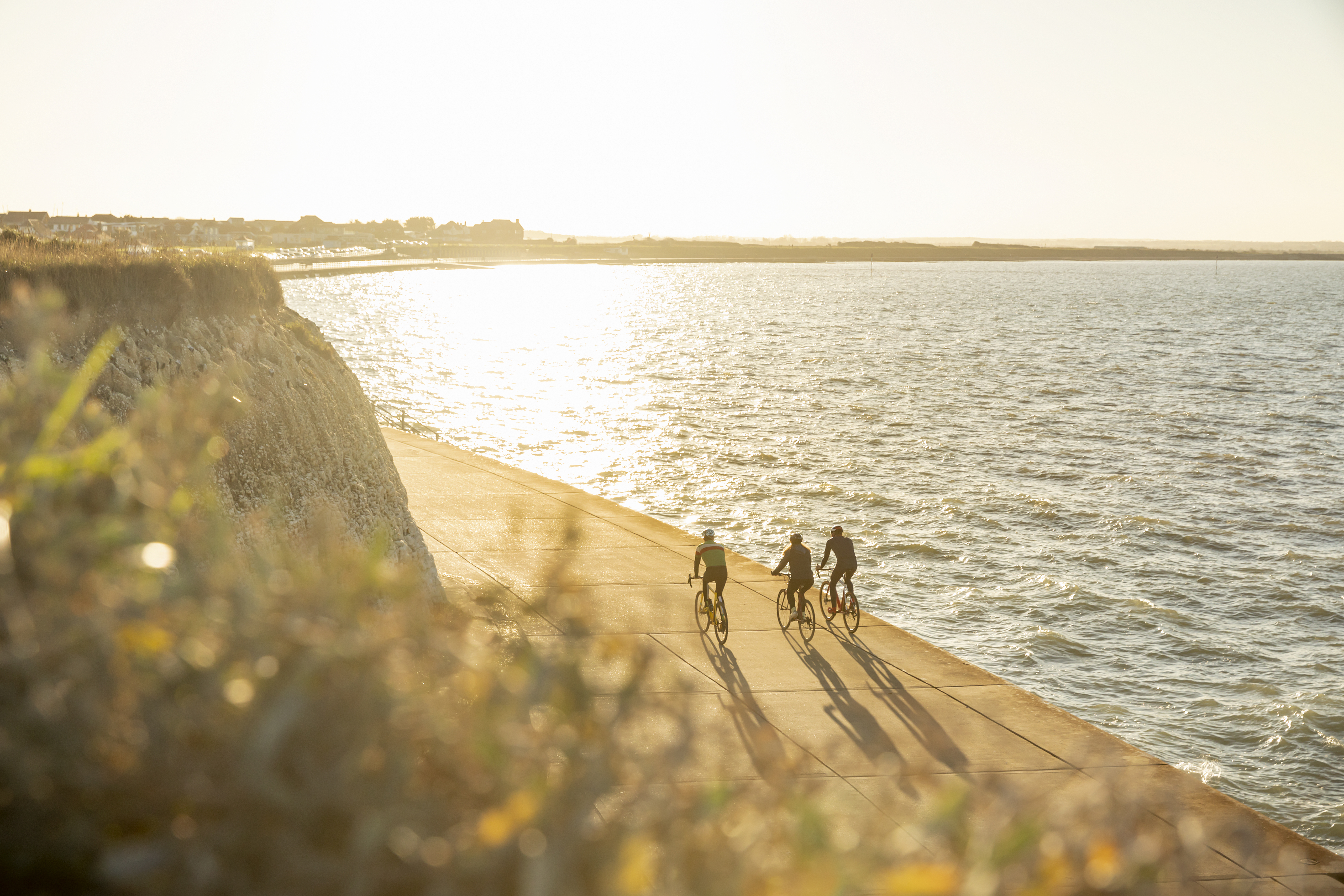 Three cyclists on a coastal path during sunset