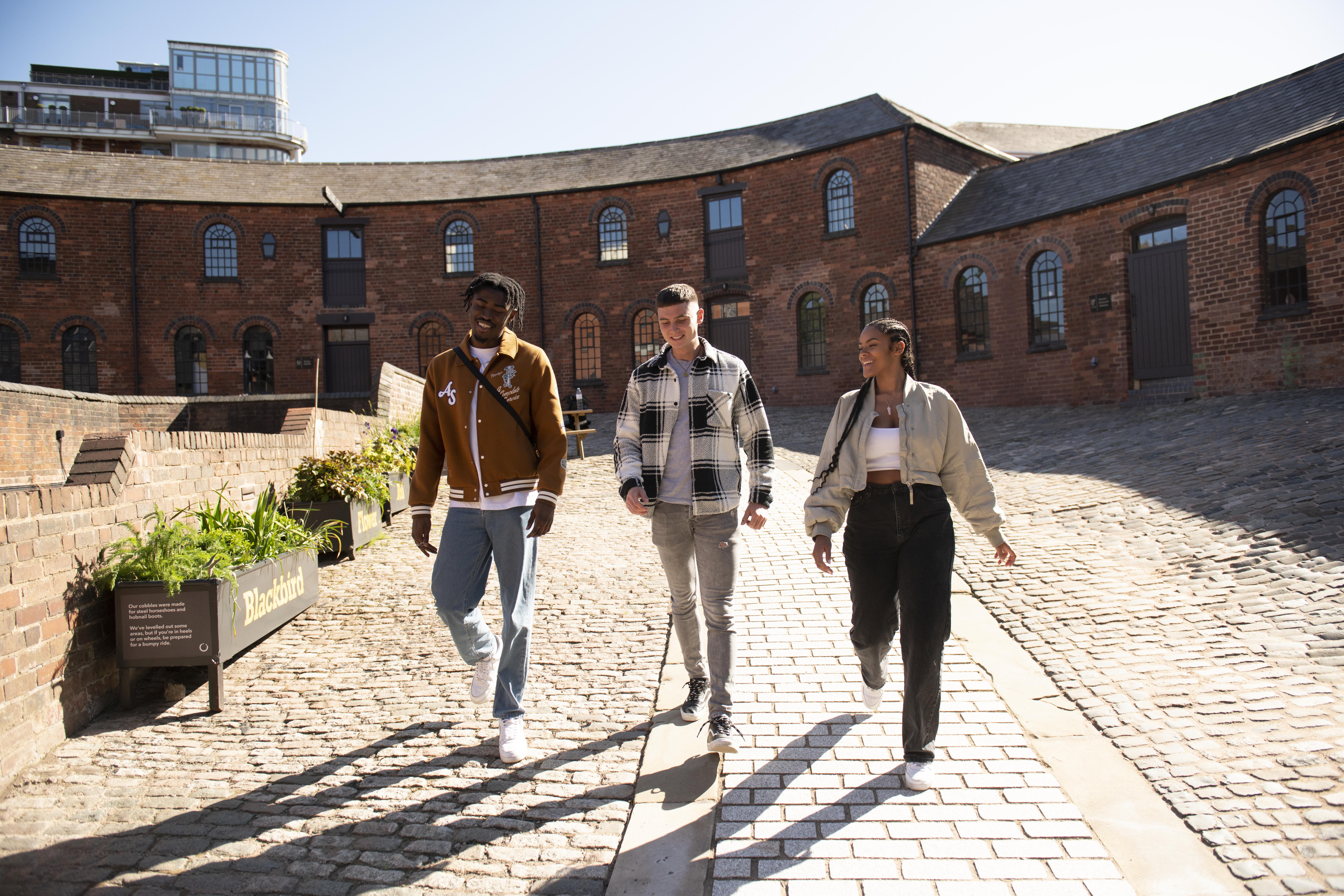 Tre amici che camminano davanti a vecchi magazzini industriali su una strada acciottolata