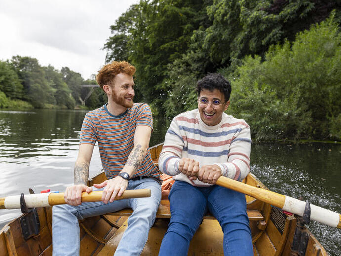 A male couple sitting in a rowboat, rowing together