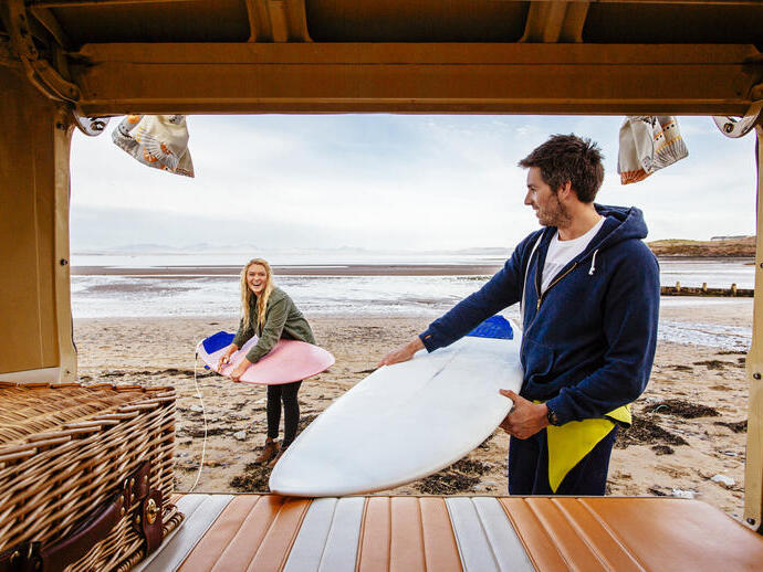 Uomo e donna che scaricano tavole da surf da un camper sulla spiaggia