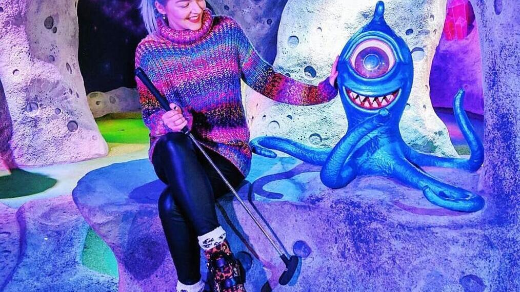 Woman smiling, holding golf club at a crazy golf venue