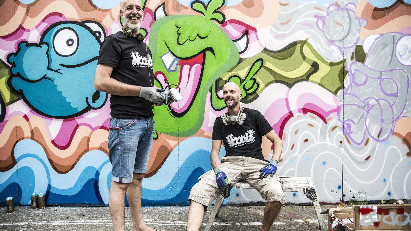 Artistas callejeros con botes de pintura cerca de coloridas obras de arte