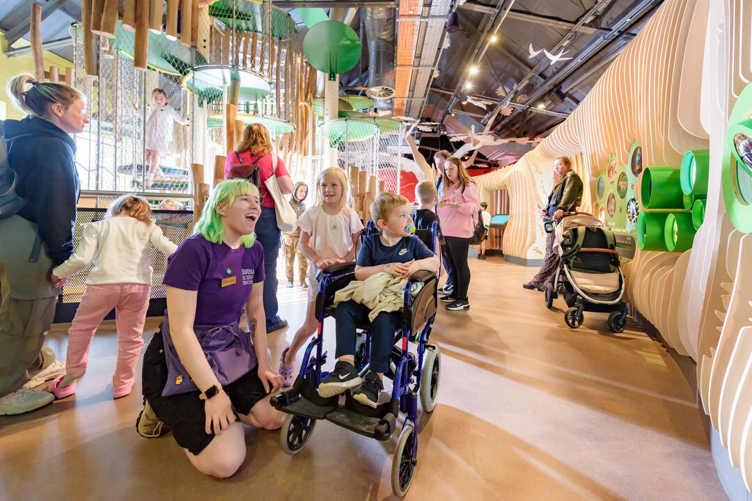 Inside a Science & Discovery Centre with children, including one wheelchair user and staff member.