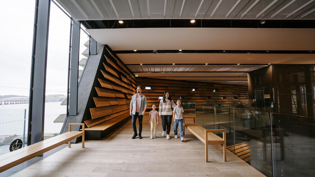 A man, a woman and two girls walking inside a modern museum.